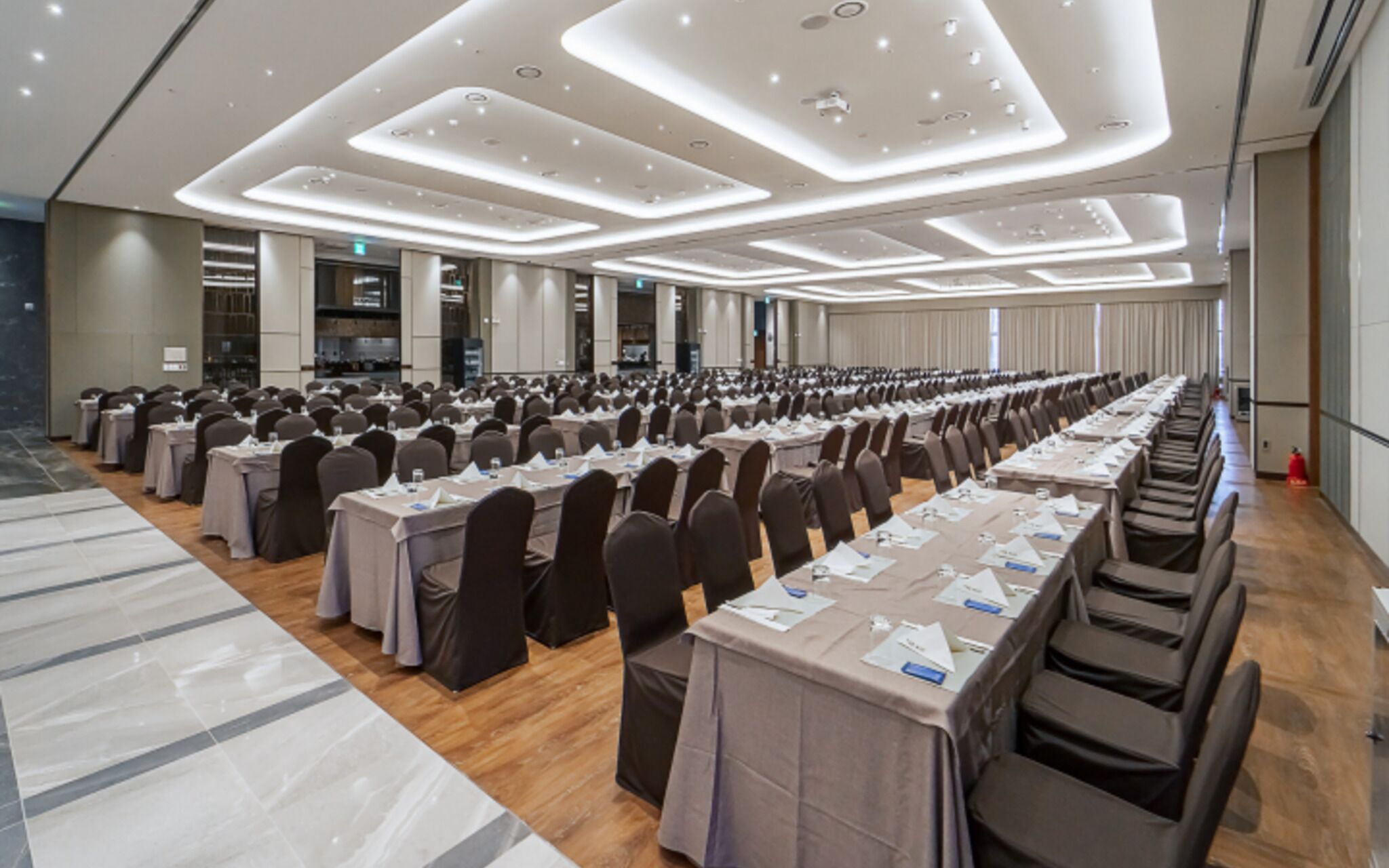 A large conference room with rows of tables and chairs, equipped with ceiling lights and a modern design.