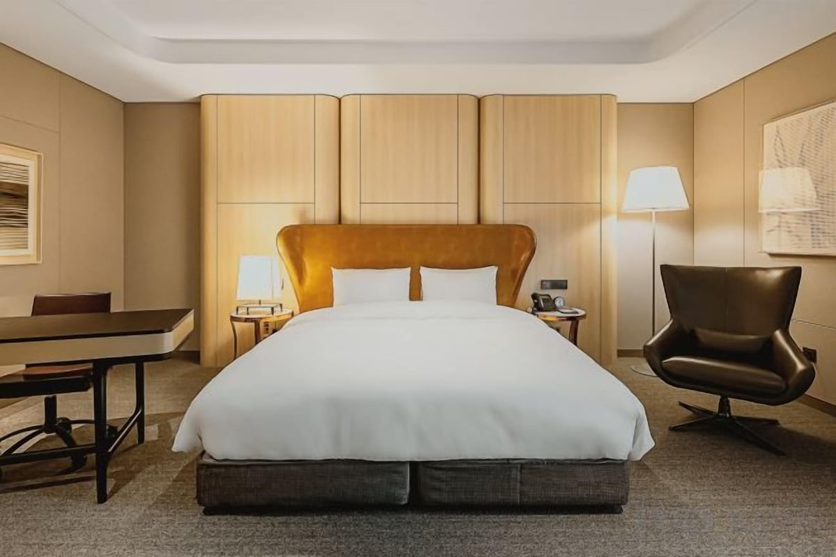 Una camera d'albergo con un letto grande, una scrivania, una sedia e una lampada.