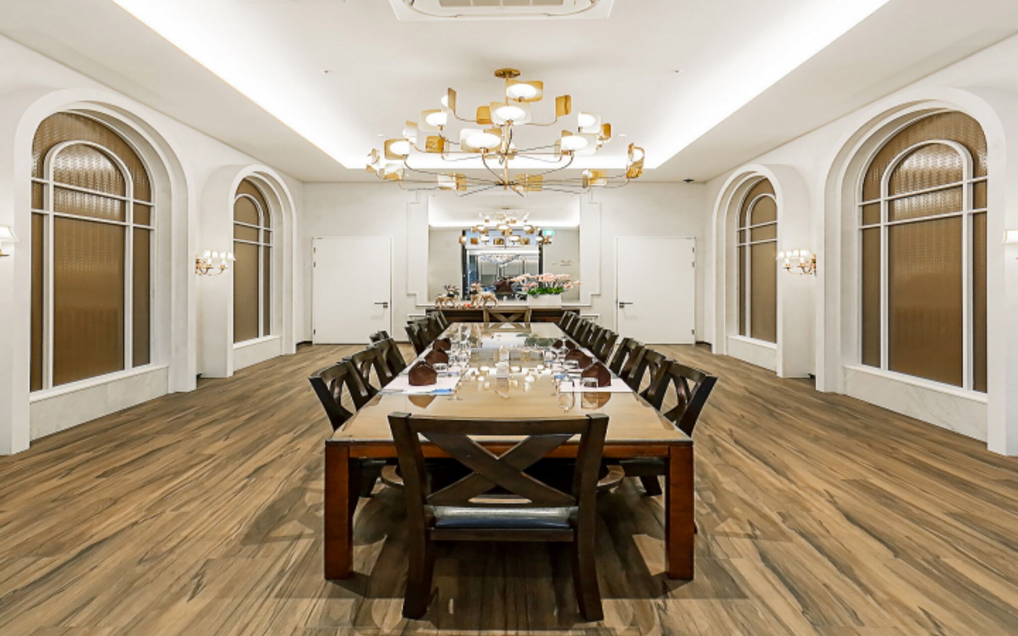 A spacious conference room with a long wooden table, multiple chairs, and a chandelier.