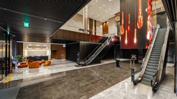 A spacious lobby with a marble floor, a staircase, and a seating area with orange chairs.