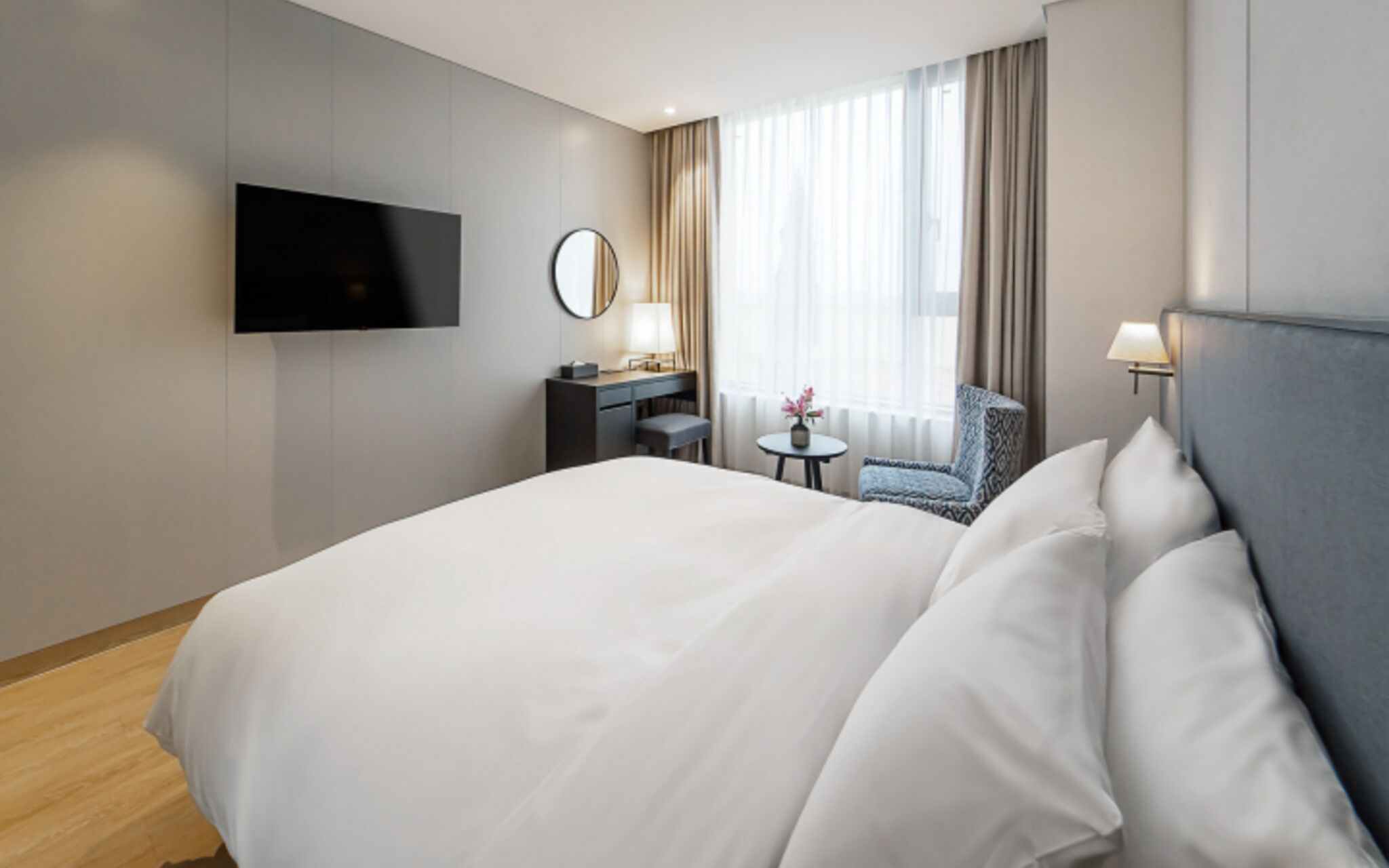 Habitación de hotel con una cama grande, un escritorio con silla, un televisor en la pared y un ventanal con cortinas.