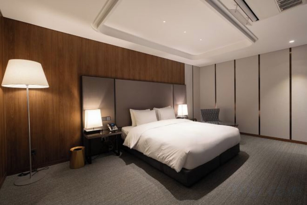 A modern hotel room with a large bed, bedside lamps, a nightstand, and a wall-mounted air conditioning unit.