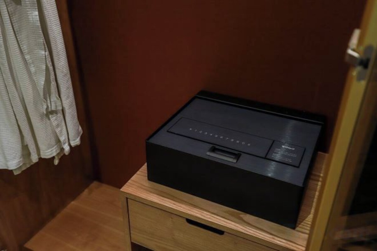 A black electronic device on a wooden nightstand in a room with a wooden door and a curtain.