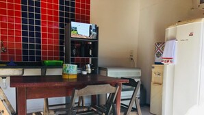 A kitchen with a wooden table, two chairs, a TV, a refrigerator, and a red tiled backsplash. - JP Estudio (RJ)