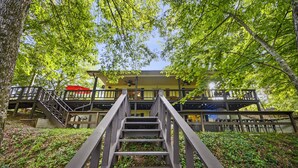 Eine Holztreppe führt zu einem überdachten Außenbereich, im Hintergrund ist ein Gebäude zu sehen.