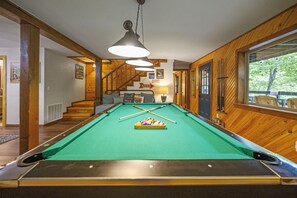 A pool table in a room with wooden walls and a staircase.