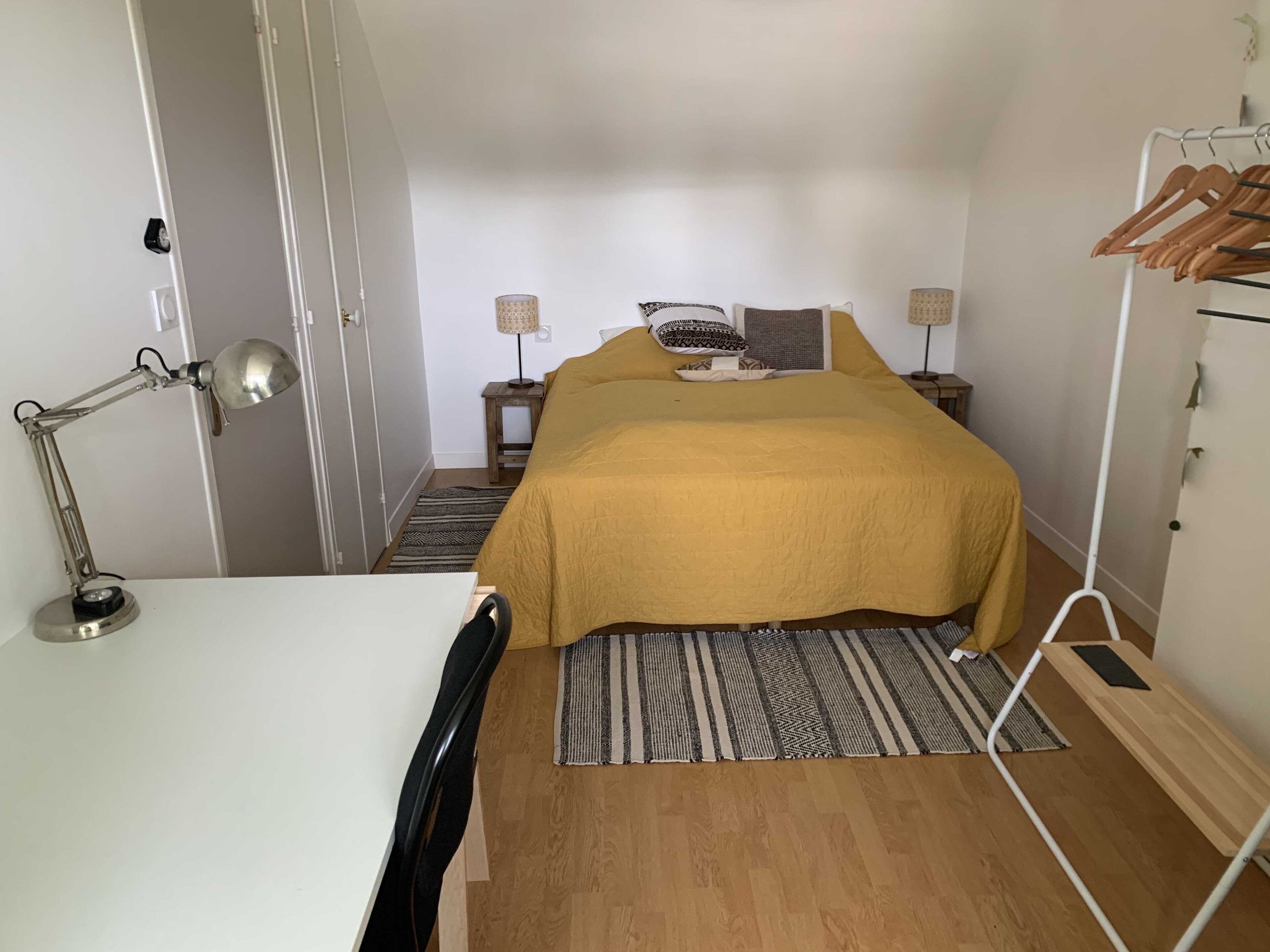 Une chambre à coucher comprenant un lit, un bureau, une chaise, une lampe et une armoire.