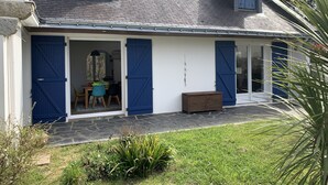 Una casa con un porche techado, un comedor con sillas y un pequeño jardín.
