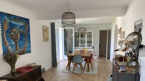 Un comedor con una mesa de madera, sillas y un jarrón de flores. Hay un cuadro en la pared y un mueble con objetos decorativos.