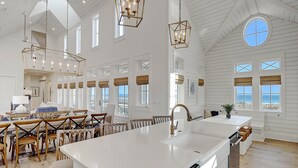 A spacious kitchen with a large island, wooden chairs, and pendant lighting.