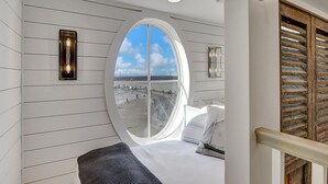 A room with a large oval window offering a view of the beach and ocean.