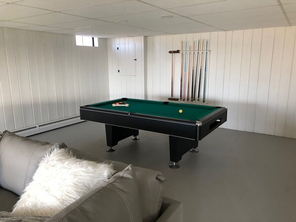 Une table de billard dans une pièce aux murs recouverts de panneaux blancs, avec un plafond blanc et une fenêtre.