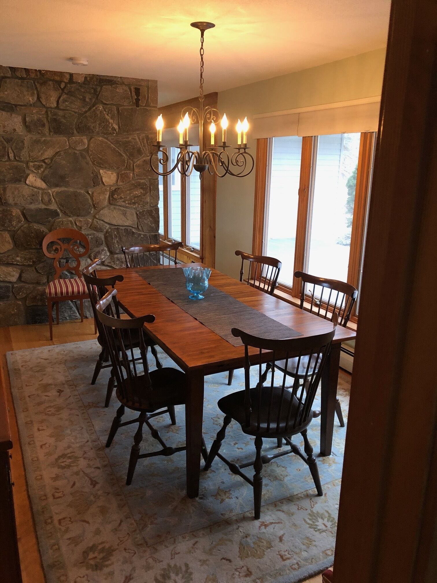 Ein Esszimmer mit einem langen Holztisch, sechs Stühlen, einer Chandelüster und einer Steinwand.