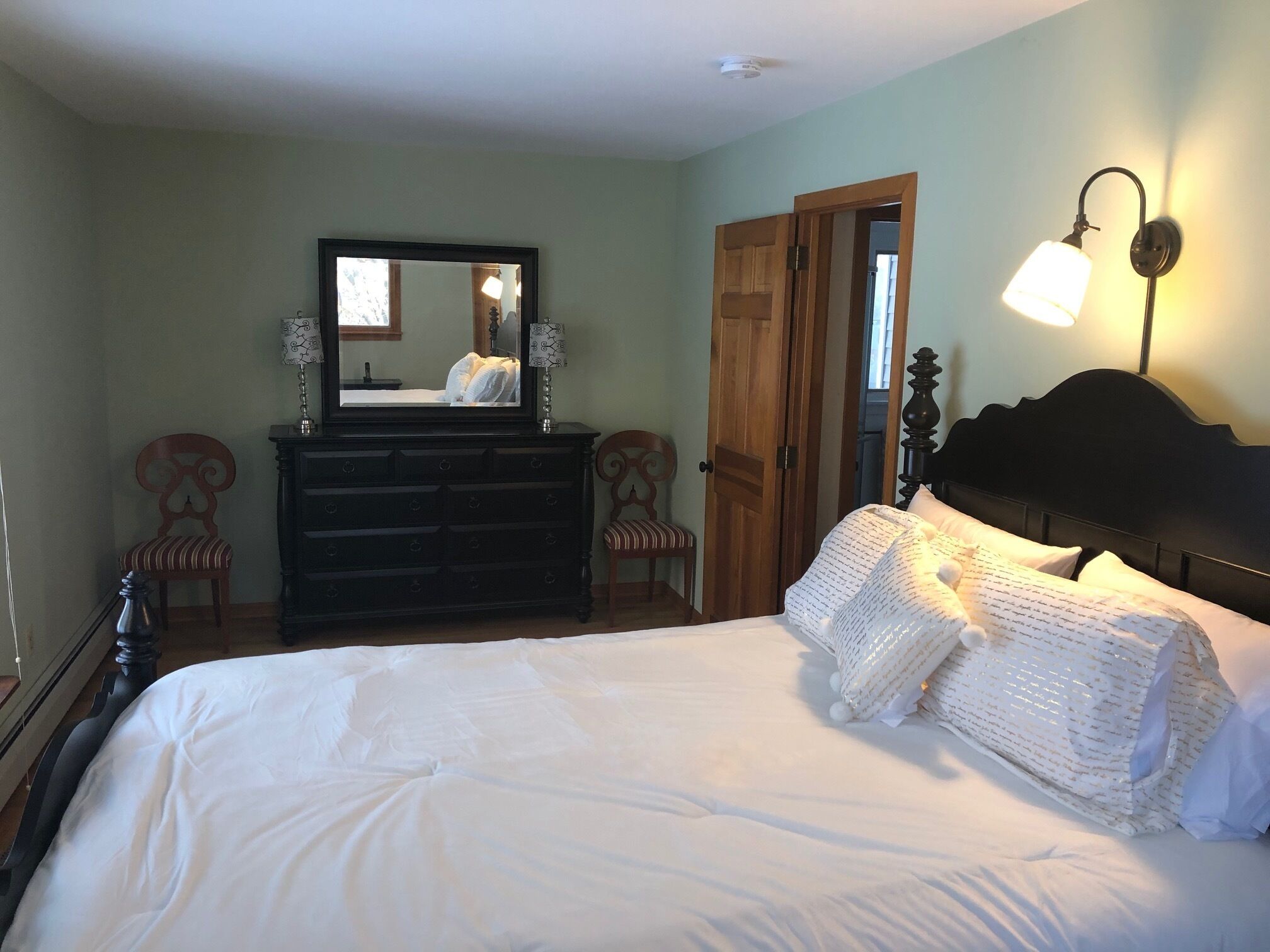 A bedroom with a bed, dresser, mirror, and wall-mounted lamp.