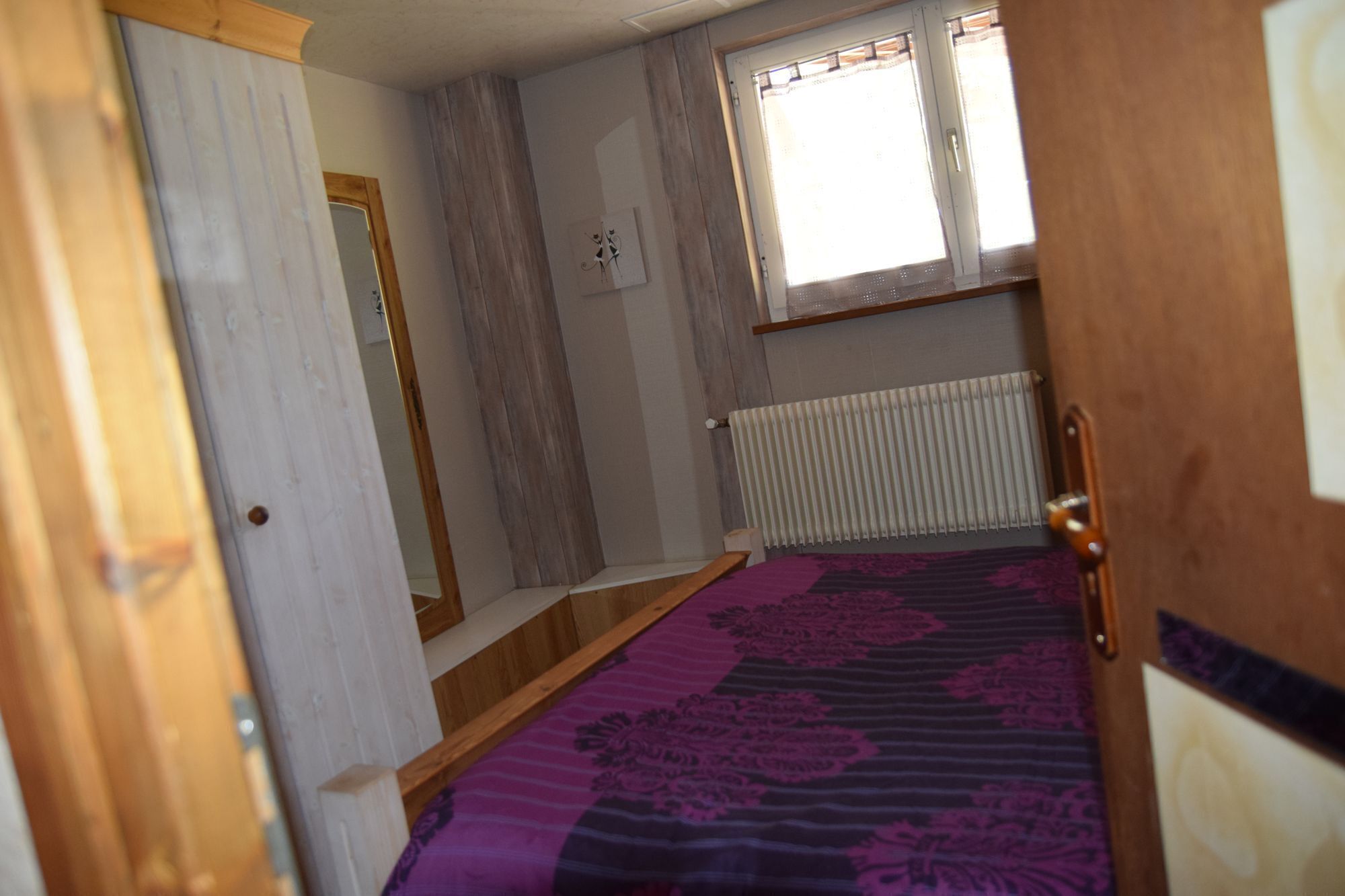 A narrow room with a wooden door, a radiator, and a window with curtains.