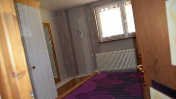A narrow room with a wooden door, a radiator, and a window with curtains.
