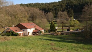 Ein Landhaus mit rotem Dach, einem kleinen Garten und einem bewaldeten Hügel im Hintergrund.