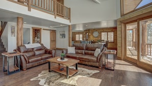 A spacious living area with a high ceiling, wooden beams, and a large window overlooking a deck. - Modern Luxury Breckenridge Cabin | Hot Tub (Breckenridge)