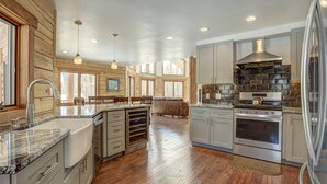 A spacious kitchen with wooden accents, a large island, stainless steel appliances, and a view of the outdoors. - Modern Luxury Breckenridge Cabin | Hot Tub (Breckenridge)