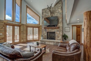A spacious living room with a stone fireplace, leather furniture, and large windows. - Modern Luxury Breckenridge Cabin | Hot Tub (Breckenridge)