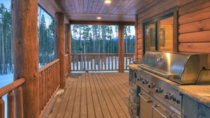 A wooden deck with a grill and a view of a snowy forest. - Modern Luxury Breckenridge Cabin | Hot Tub (Breckenridge)
