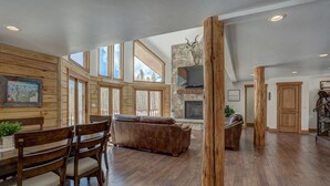 A spacious living area with a stone fireplace, wooden furniture, and large windows offering views of the outdoors. - Modern Luxury Breckenridge Cabin | Hot Tub (Breckenridge)