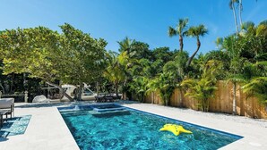 A rectangular swimming pool with clear blue water, surrounded by a wooden fence and lush greenery. - Waterfront Pool Home Steps to Beach (Bradenton Beach)