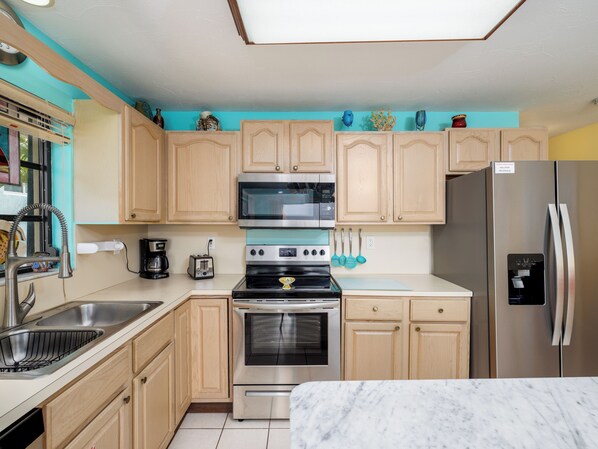 A modern kitchen with wooden cabinets, stainless steel appliances, and a marble countertop. - Turquoise Lagoon LLC, wide open turquoise views of the lagoon (Key Colony Beach)