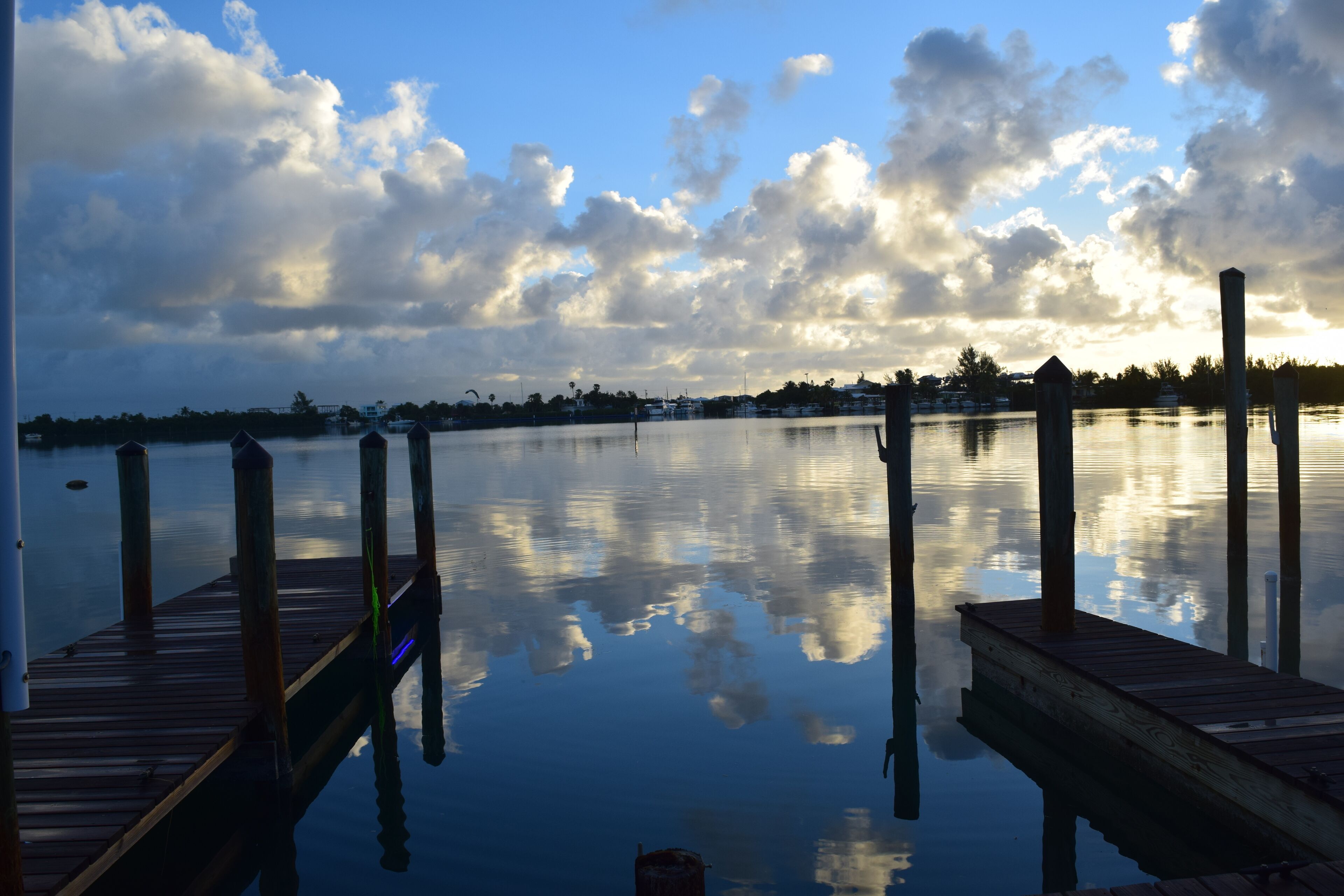 A wooden dock extending into calm water with a clear sky and clouds reflected on the surface.