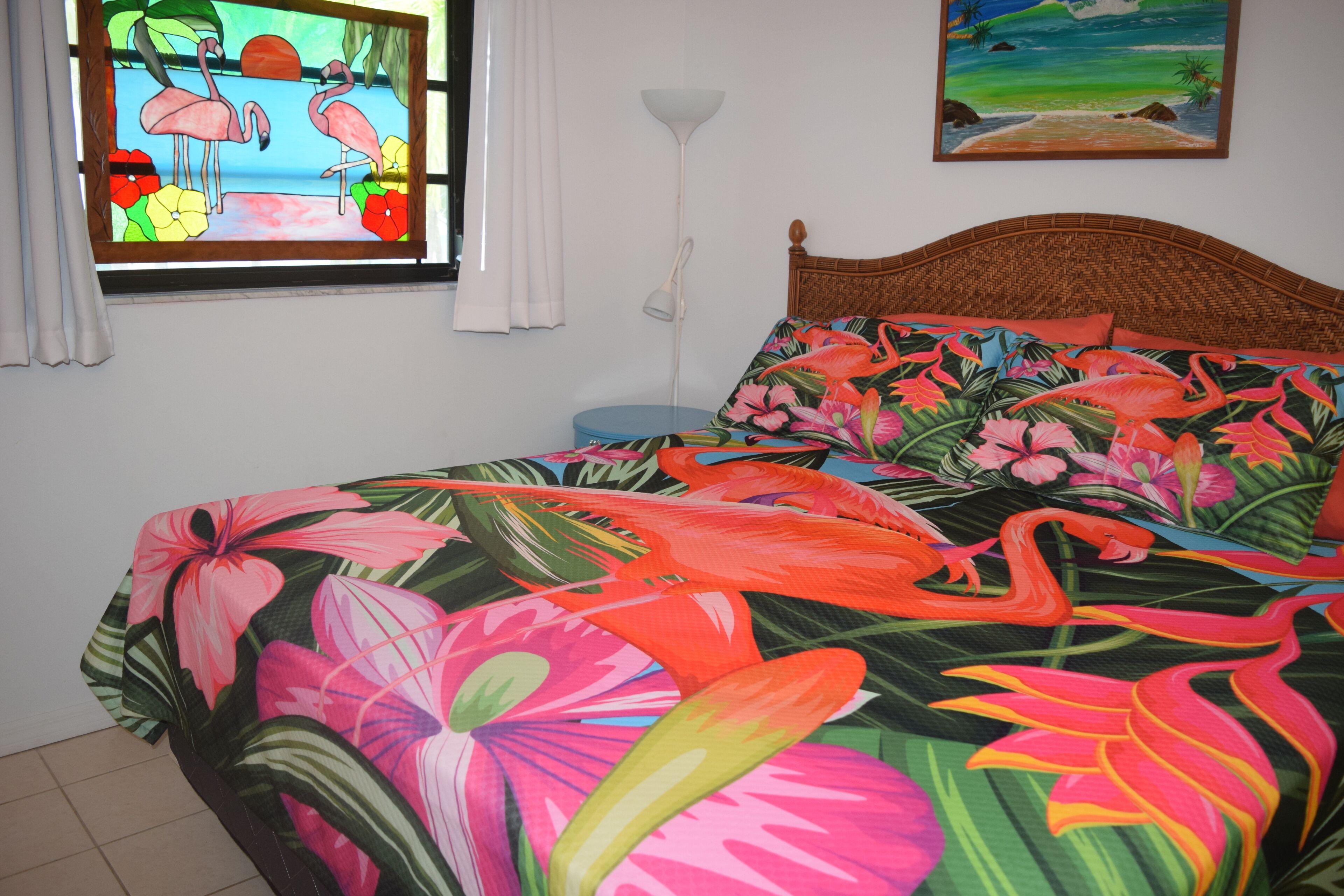 A bed with a floral bedspread, a nightstand, a lamp, and a painting on the wall.