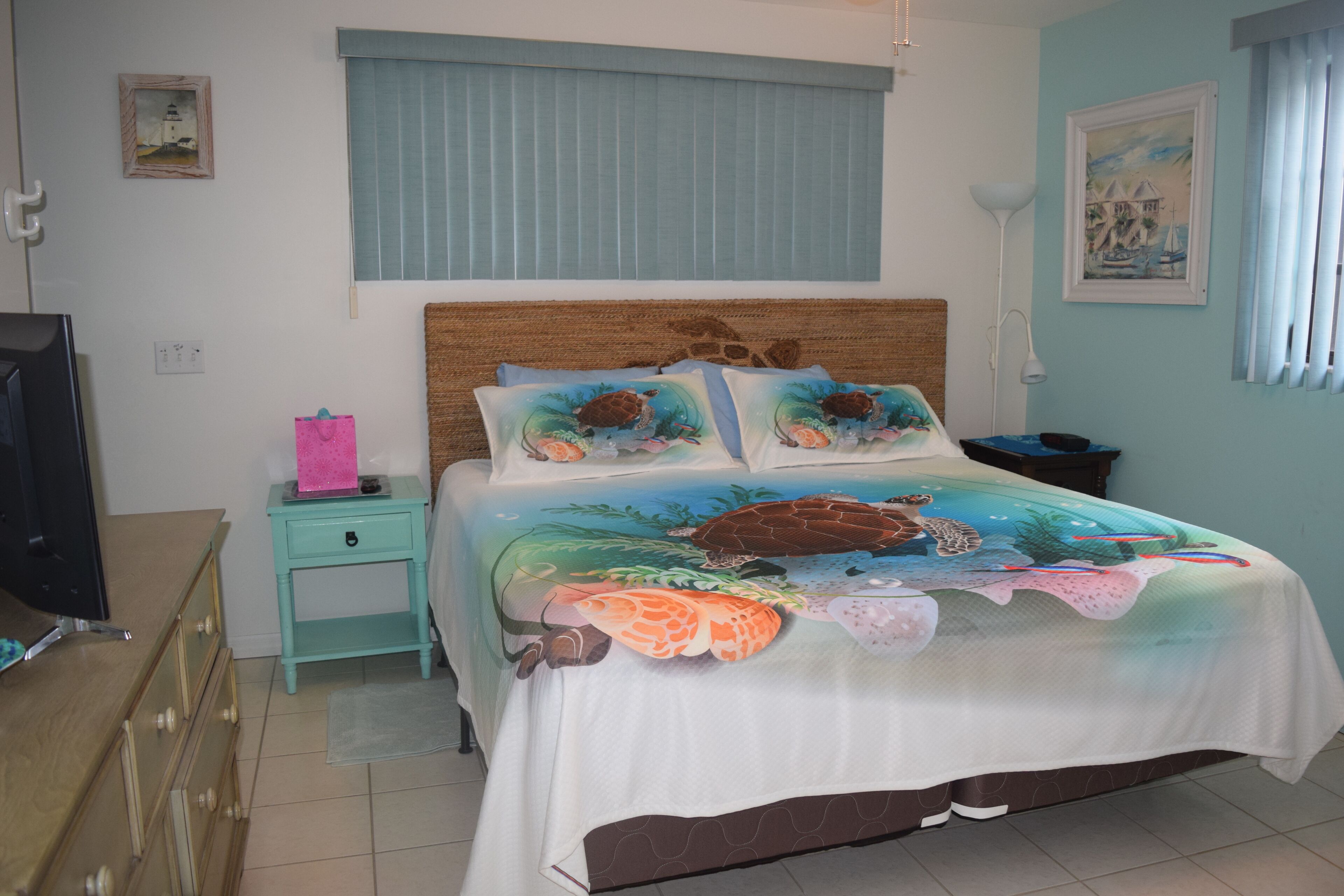 A bedroom with a bed, a nightstand, a dresser, a lamp, and a painting on the wall.