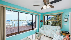 Une pièce dotée d’une grande fenêtre, d’un ventilateur de plafond, d’un canapé, d’une petite table et offrant une vue sur un quai et des bateaux.