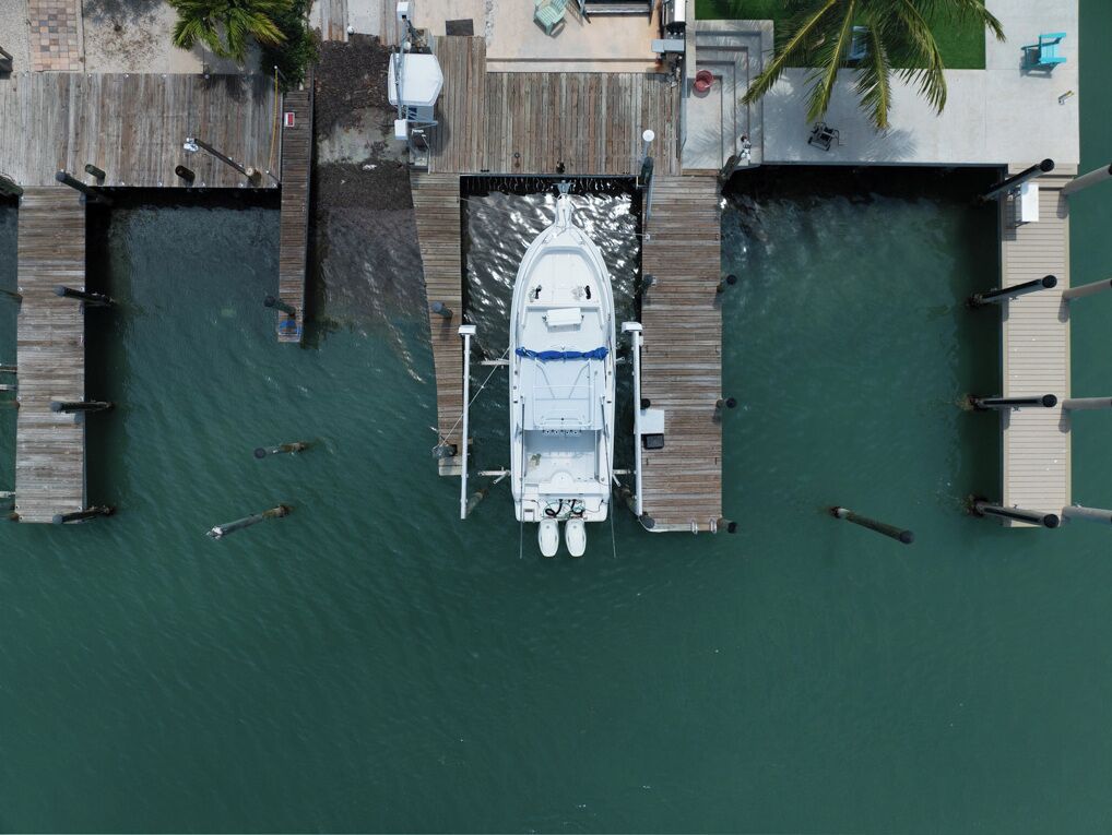Vue aérienne d’un quai avec un bateau, des passerelles en bois et un petit bâtiment.