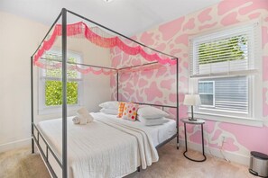 A four-poster bed with a canopy, a bedside table with a lamp, and a wall with a pink and white abstract pattern.