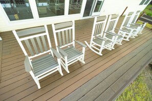 Eine Holzterrasse mit weiß gestellten Adirondack-Stühlen in einer Reihe.