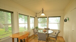 A dining area with a wooden table and chairs, large windows, and a hanging light fixture. - Large house on beautiful lake, adjoins Sleeping Bear Dunes National Lakeshore (Empire)
