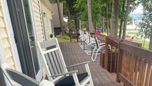 A wooden deck with white rocking chairs and a wooden railing. - Large house on beautiful lake, adjoins Sleeping Bear Dunes National Lakeshore (Empire)