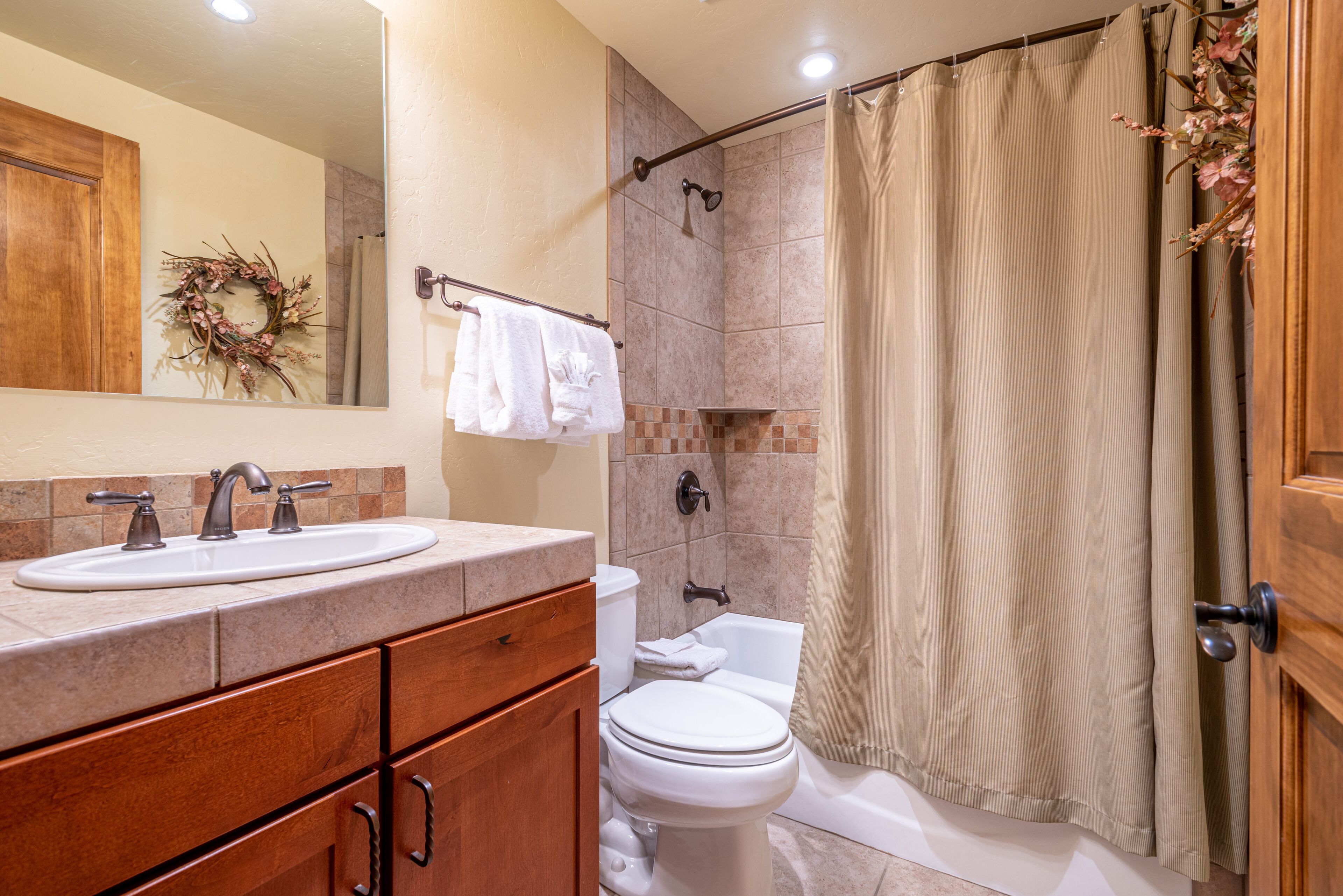 A bathroom with a sink, mirror, wooden cabinet, toilet, and shower curtain.