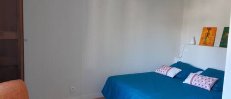 Un dormitorio con cama, una silla, una lámpara de techo blanca y una pared con dos cuadros.