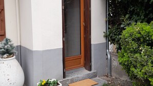 Una casa con una porta in legno, un piccolo portico e un vaso con una pianta.