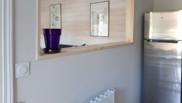 Una cucina con un frigorifero in acciaio inossidabile, uno scaffale in legno con un contenitore viola e quadri appesi al muro.