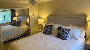 Camera d'albergo con due letti, una ventola a soffitto e un'ampia finestra con tende.