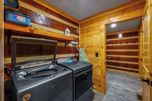 Ein kompakter Hauswirtschaftsraum mit einer Waschmaschine und einem Trockner, Holzvertäfelung und einem kleinen Regal mit einem blauen Behälter.