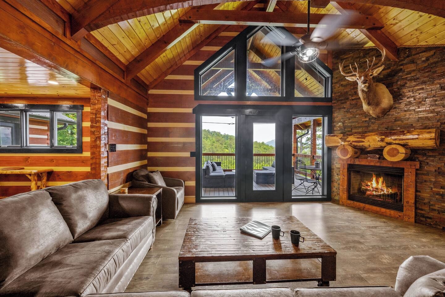 A log cabin interior with a fireplace, leather sofa, and a view through the glass doors.