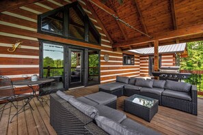 A covered outdoor area with a wooden deck, a dining table with chairs, a sofa, and a grill.