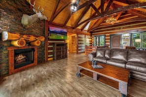 A rustic interior with a fireplace, leather sofa, and a mounted deer head.