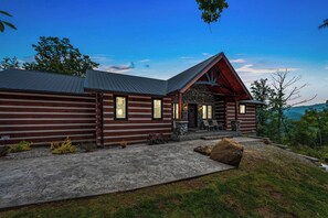 A log cabin with a stone porch, a concrete driveway, and a view of the surrounding landscape.