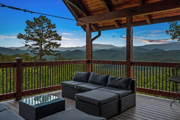 A covered outdoor seating area with a sofa and chairs, overlooking a mountainous landscape.