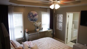 A bedroom with a bed, a dresser, a ceiling fan, and a bathroom door. - The Establishment (Atl)
