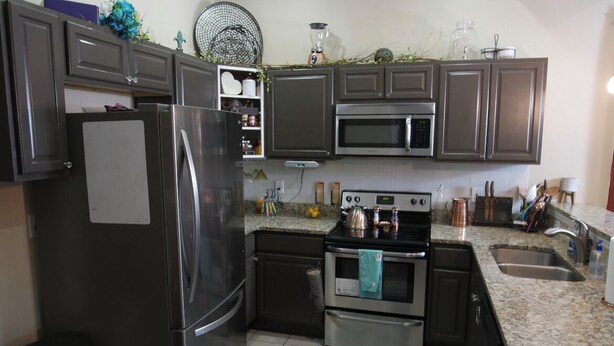 A modern kitchen with stainless steel appliances, granite countertops, and dark cabinetry. - The Establishment (Atl)